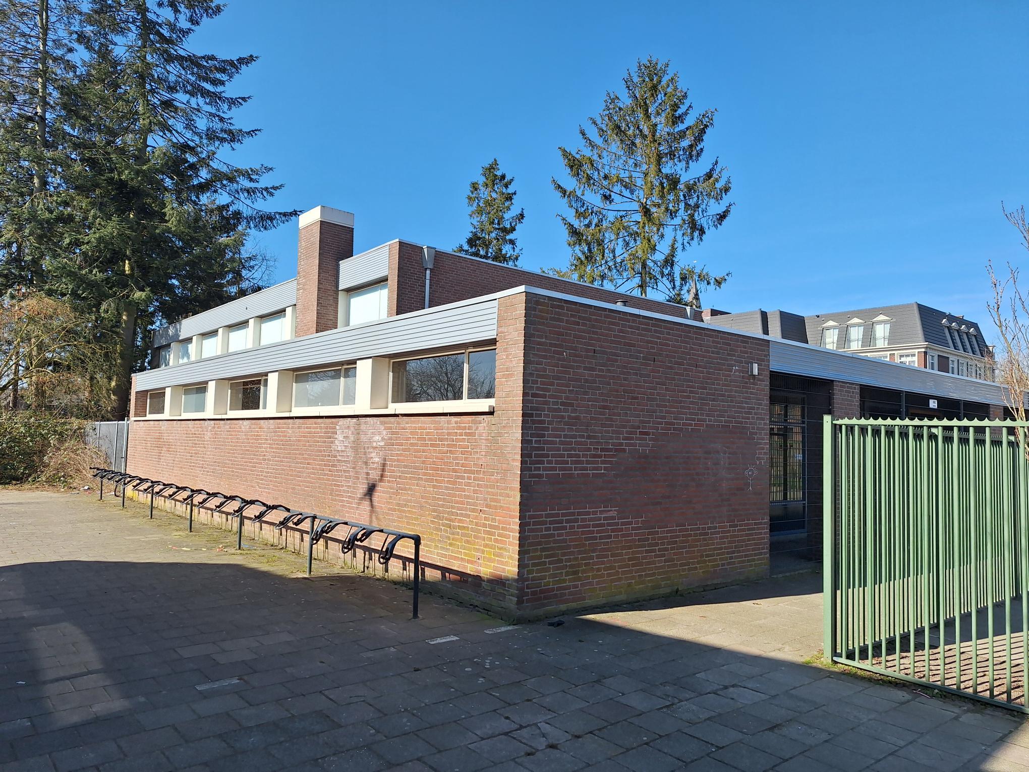 bakstenen gebouw met hoge ramen en groen hek