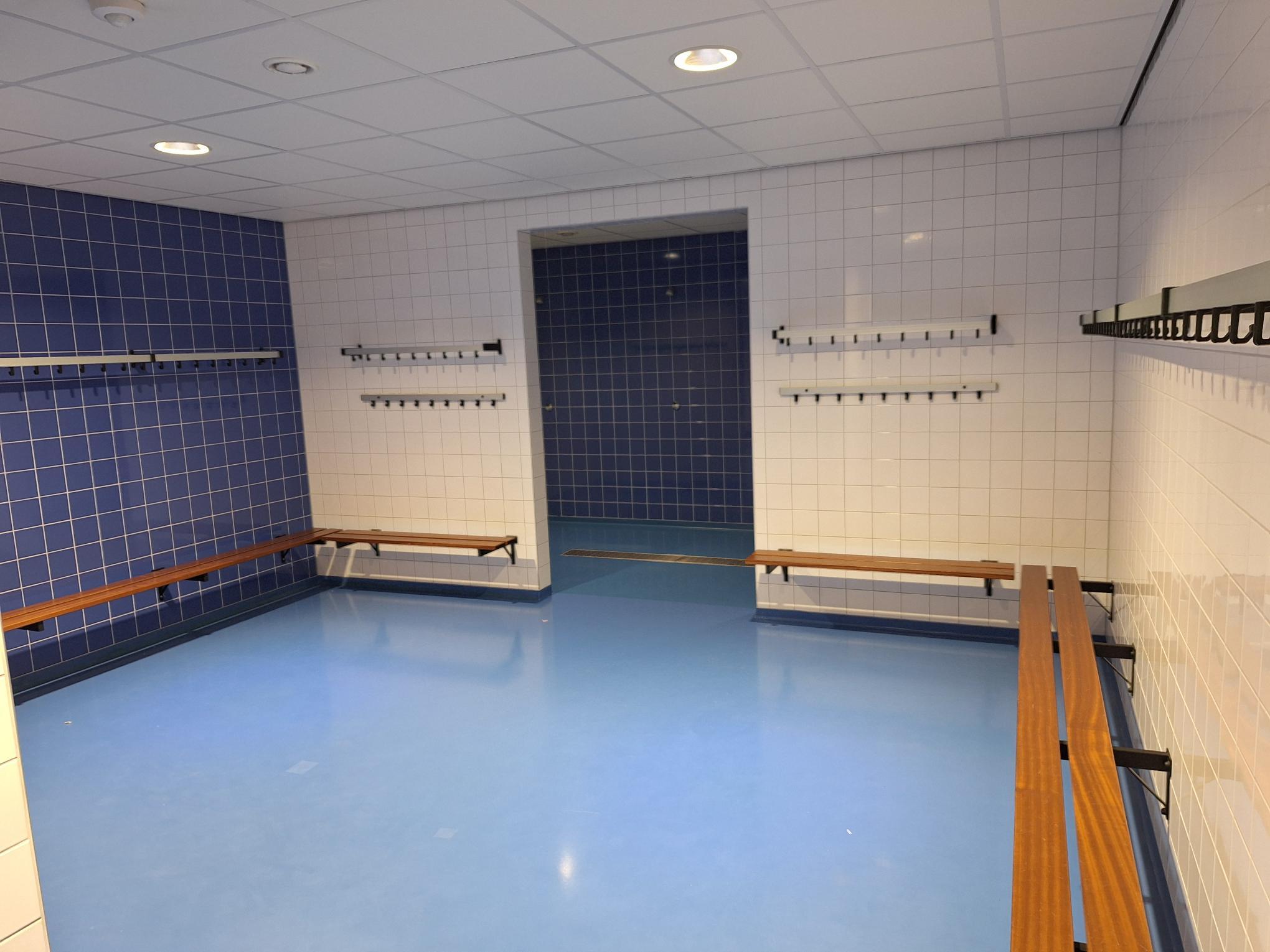 binnenruimte met helderblauwe vloer en houten bankjes tegen de muur