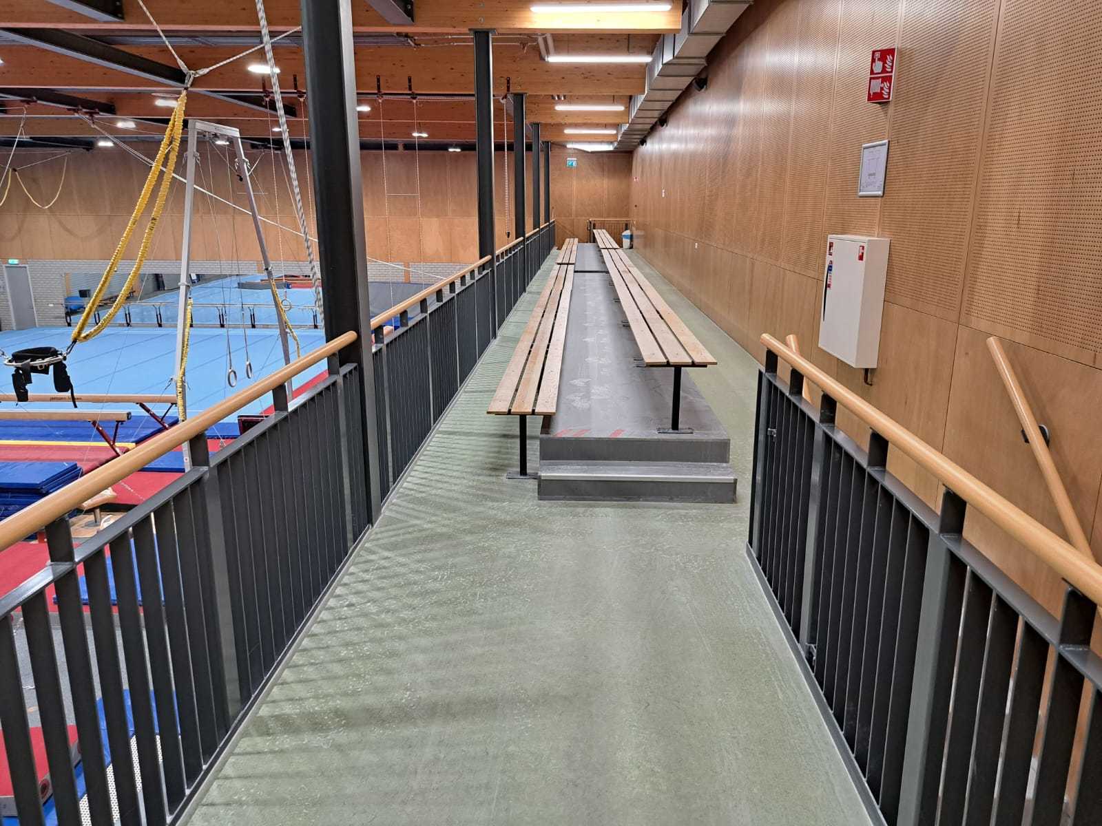 Lange houten banken op verhoging die uitkijken op turnhal