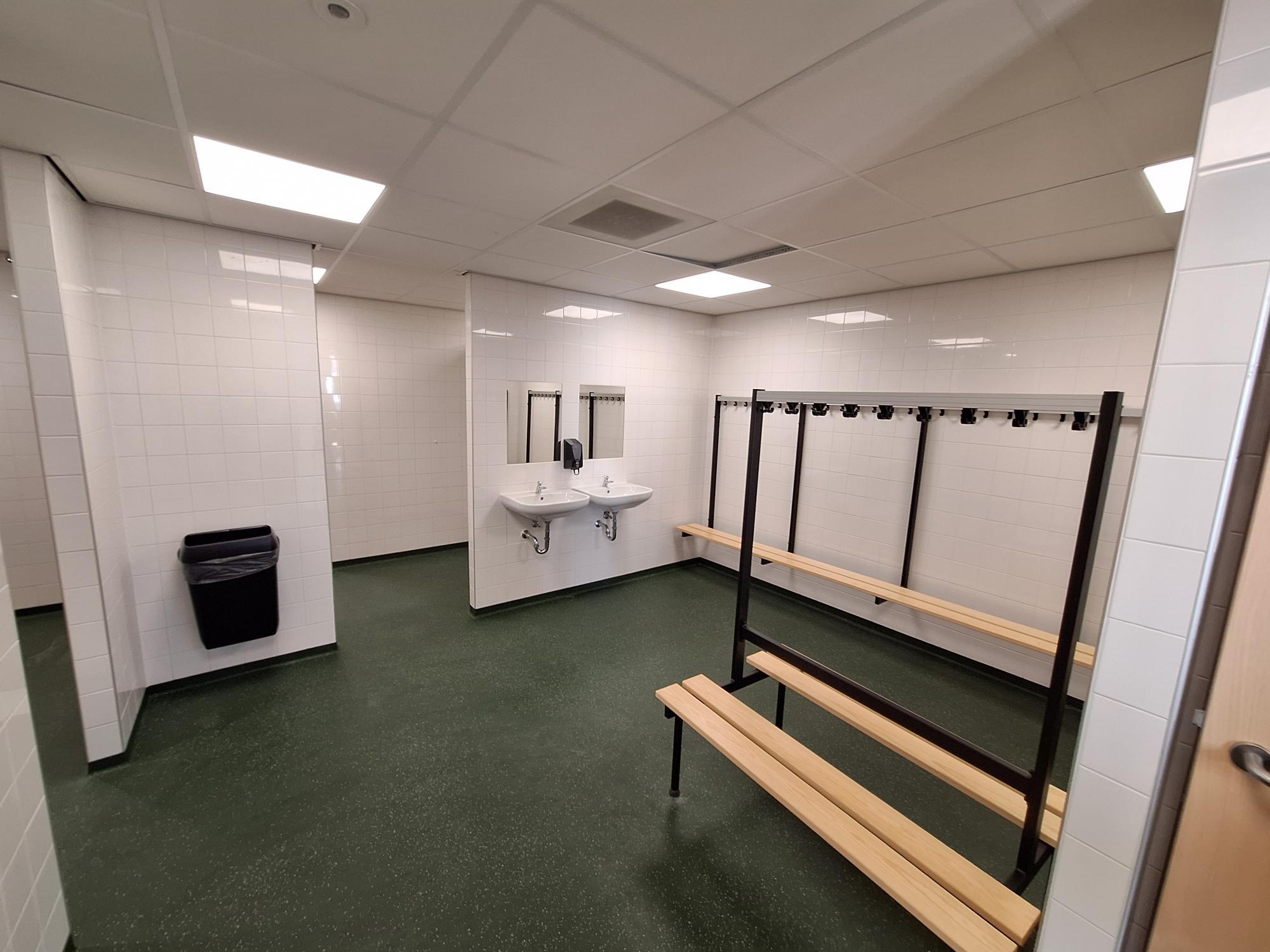 ruimte met witte tegelwanden, douches en houten bankjes