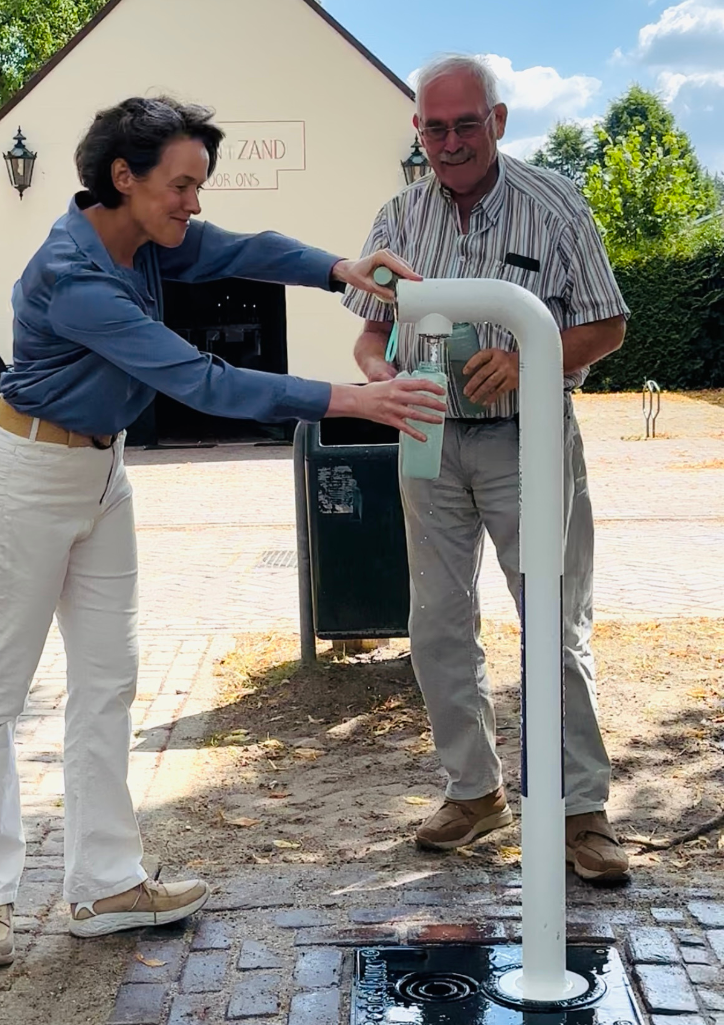 Wethouder Mariëlle Giesbertz en Gerrit Coppens, raadslid Senioren Veldhoven vullen hun flesje bij het watertappunt in Zandoerle.