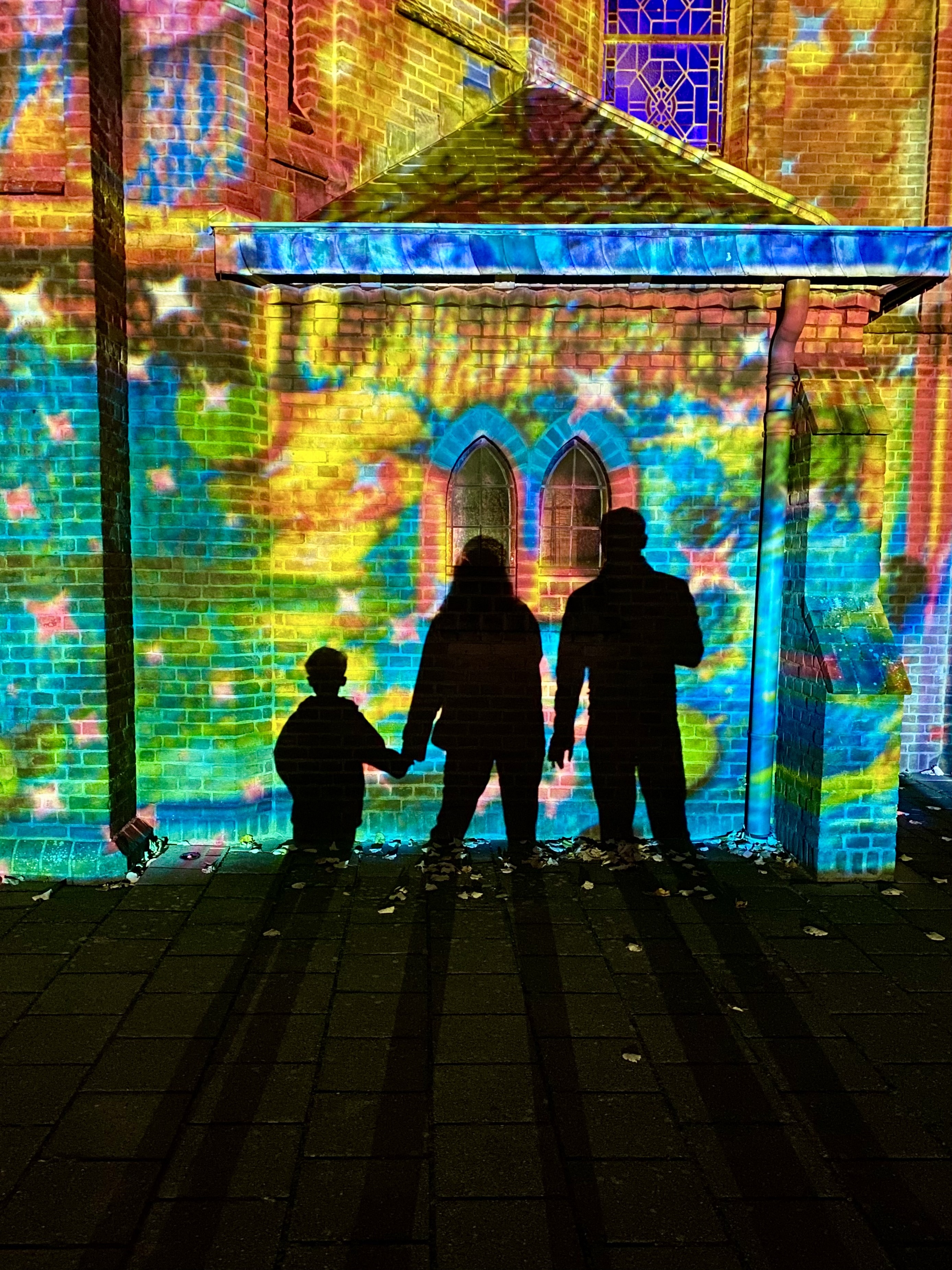 GLOW Veldhoven, silhouet van gezin, vrouw houdt hand vast van kind voor de Sint-Caeciliakerk,